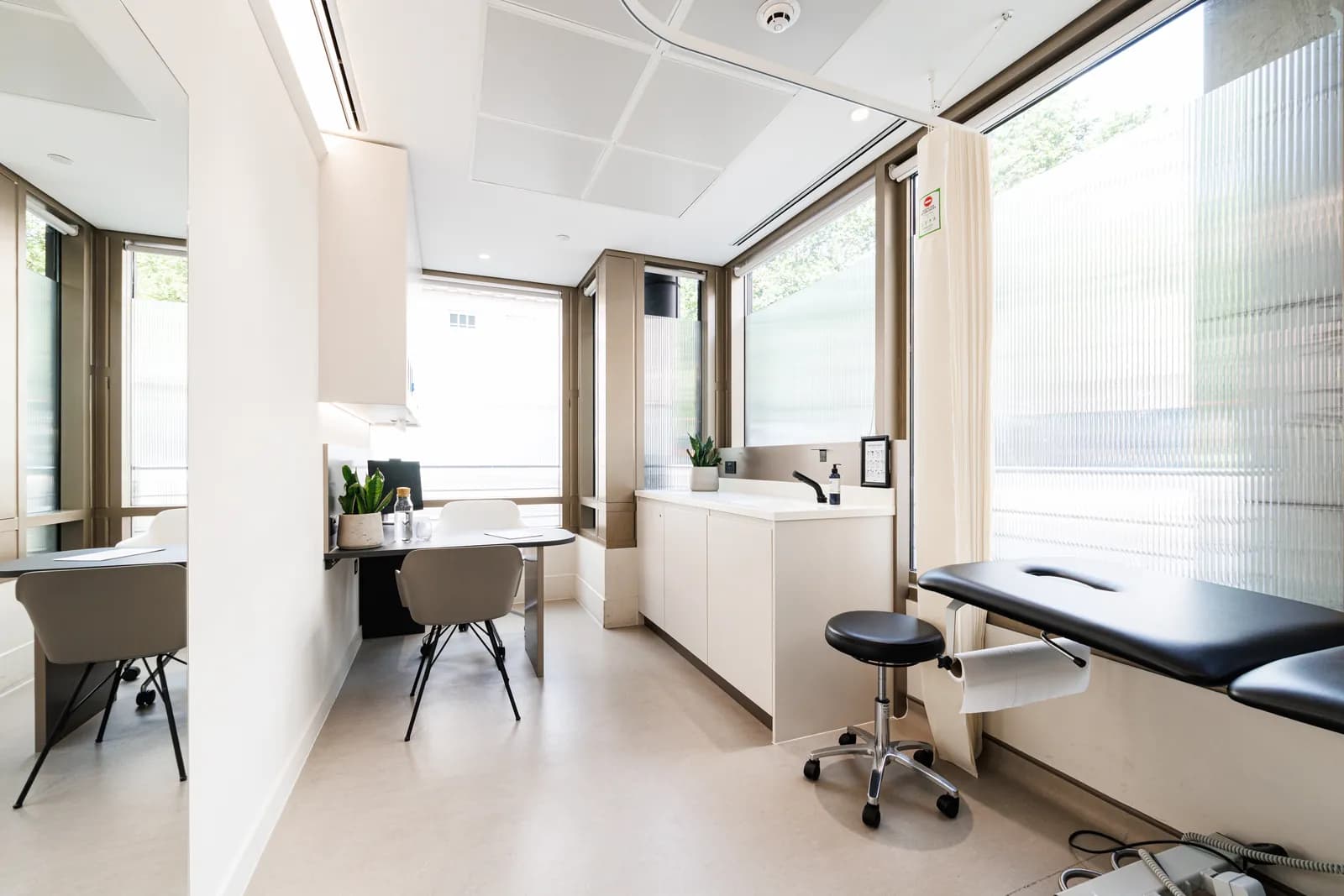 Bright treatment room at Atlas Osteopathy Bond Street with adjustable plinth, consultation desk and floor-to-ceiling windows.