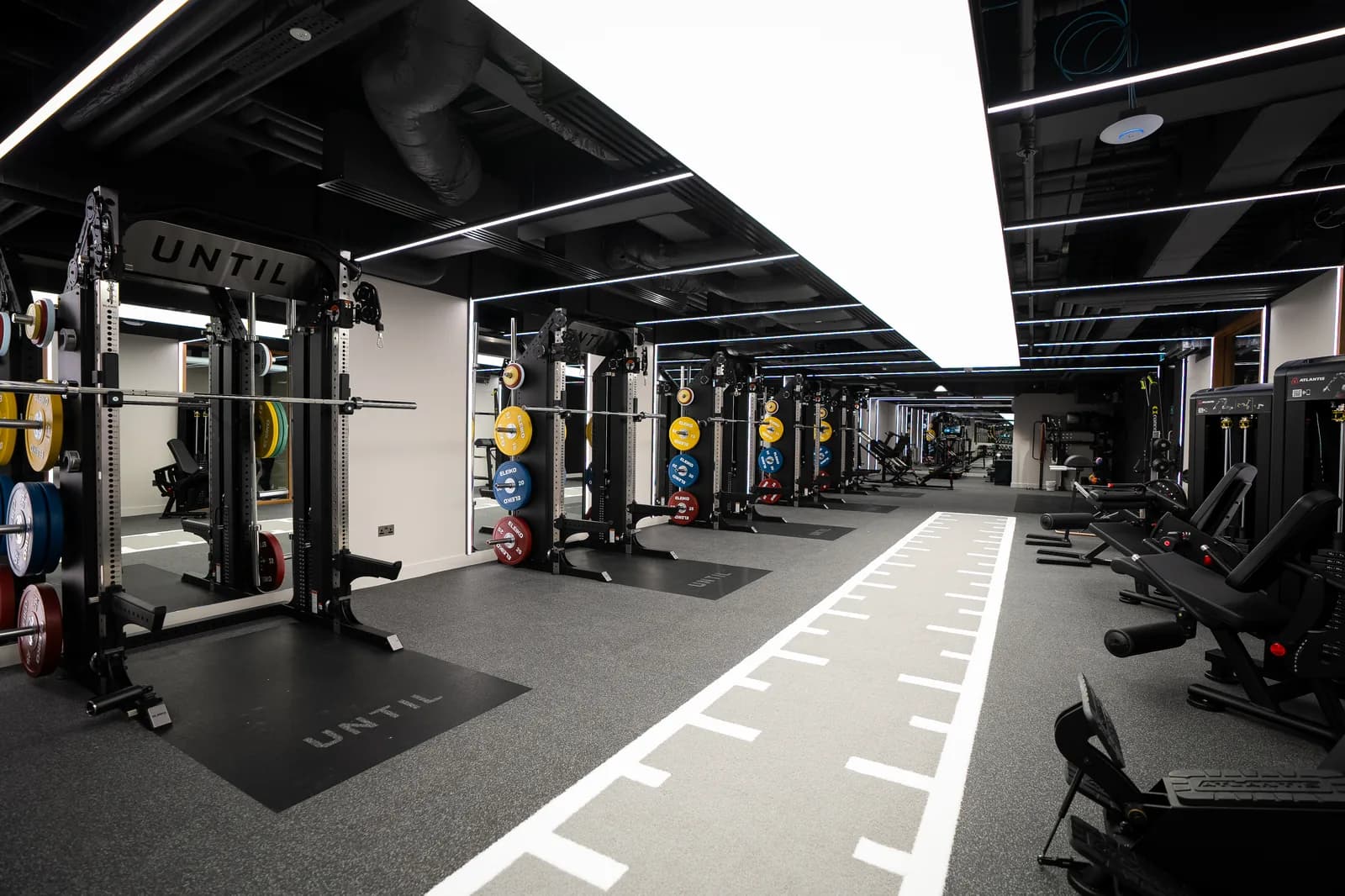 UNTIL Canary Wharf gym floor with squat racks, plate-loaded weights and a sprint track.