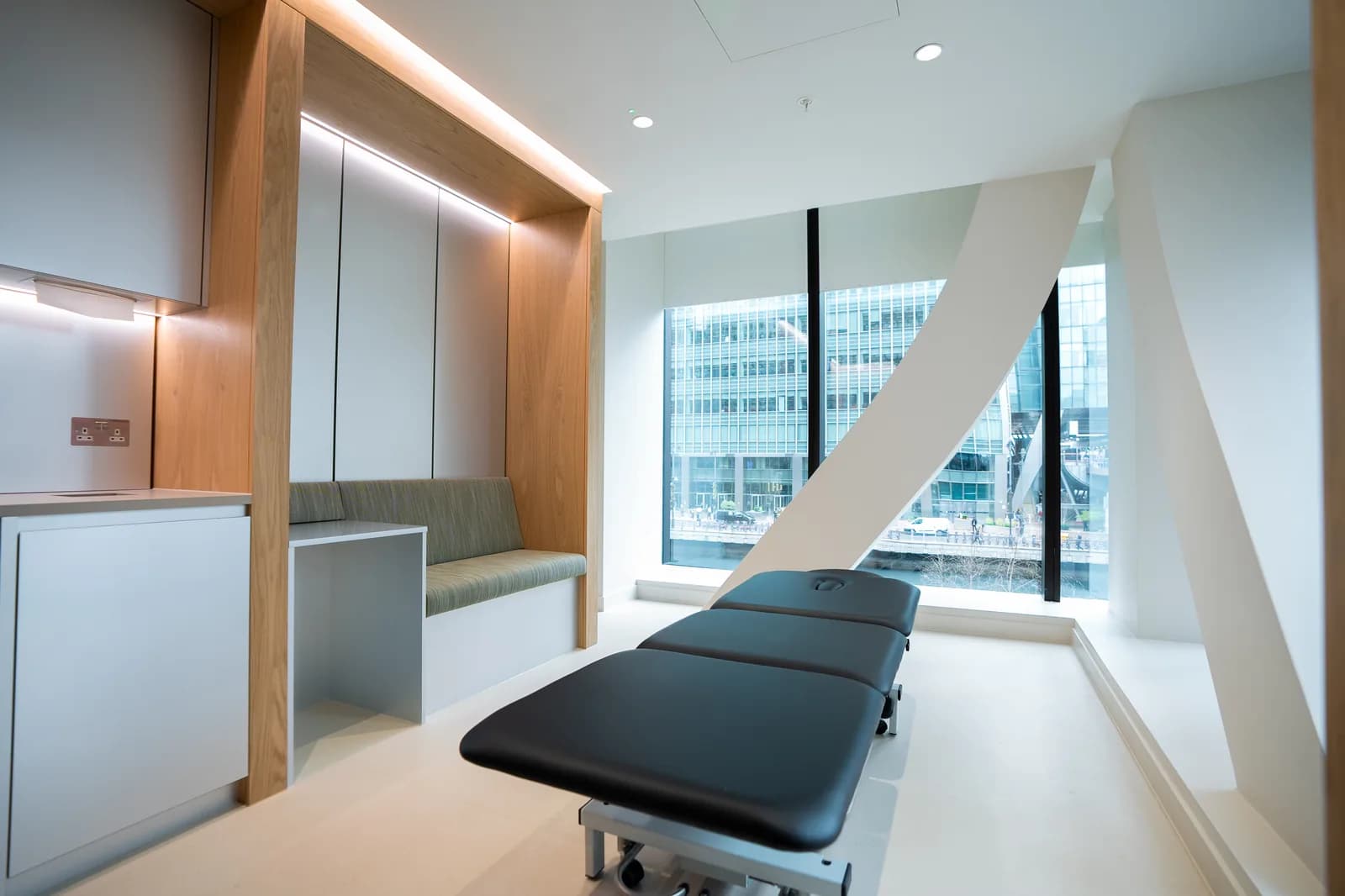 Atlas Osteopathy Canary Wharf treatment room overlooking the Wharf skyline through floor-to-ceiling glass.