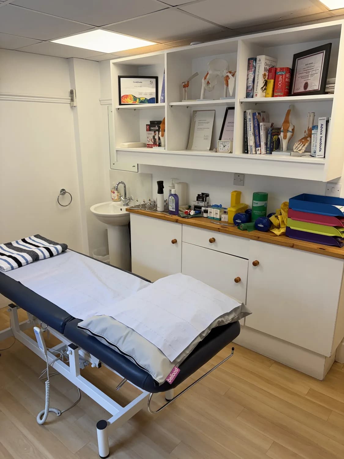 Treatment room at Atlas Osteopathy Finchley with adjustable plinth and anatomy reference models on the shelves.